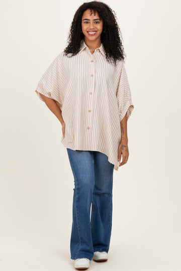 woman wearing a beige striped oversized button-up shirt with rolled sleeves and blue flared jeans