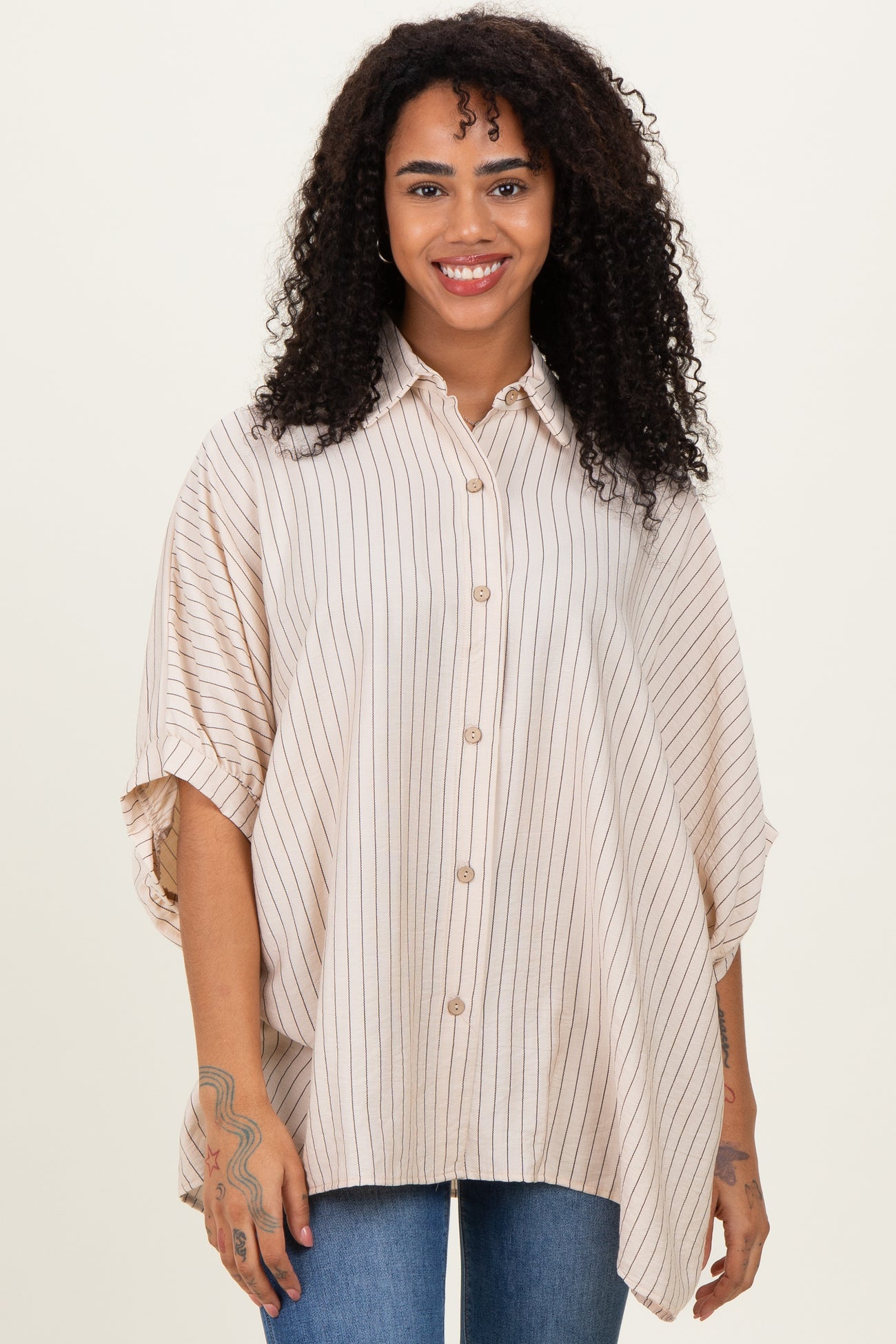 woman wearing a beige striped oversized shirt with short sleeves and button front, smiling at the camera
