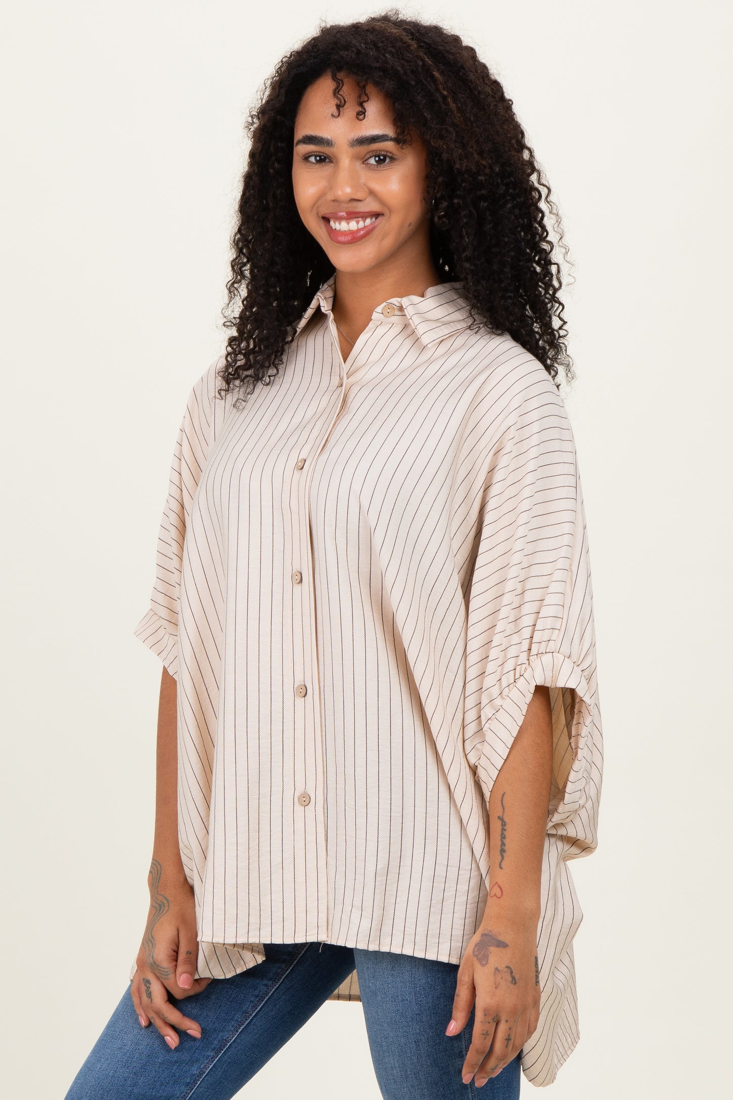 woman wearing a beige and cream striped oversized button-up shirt paired with blue jeans