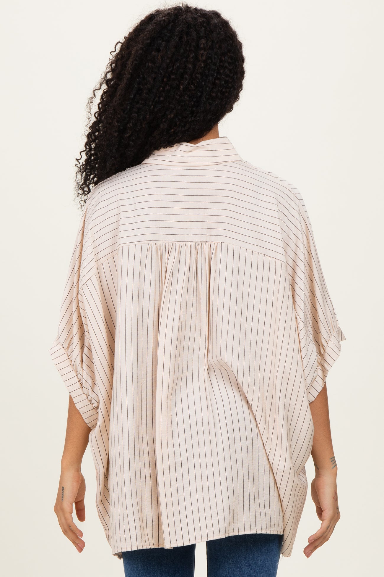 woman showing the back of a beige striped oversized blouse with short sleeves and a relaxed fit