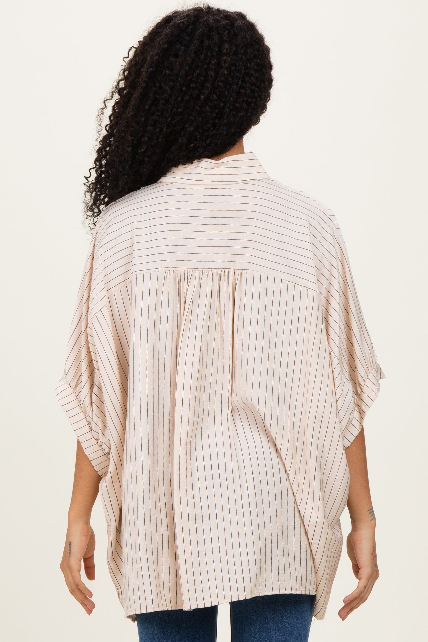 woman showing the back of a beige striped oversized blouse with short sleeves and a relaxed fit