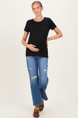 woman wearing a black short sleeve maternity top and distressed blue jeans, gently holding her baby bump