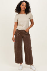 woman wearing a beige short sleeve top and brown wide-leg corduroy pants, standing with one hand on her hip