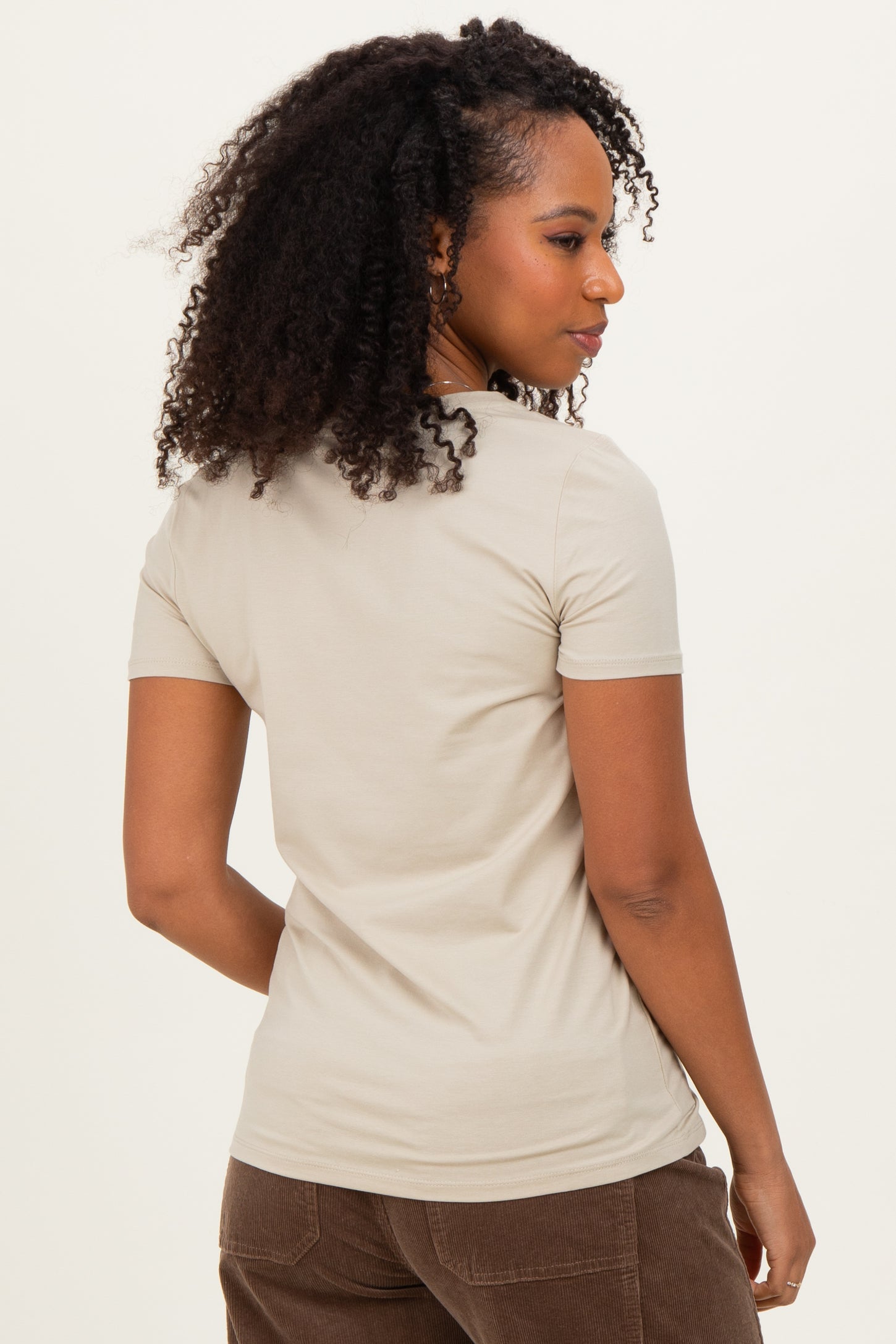 woman wearing a light beige short sleeve t-shirt, facing away from the camera with curly hair