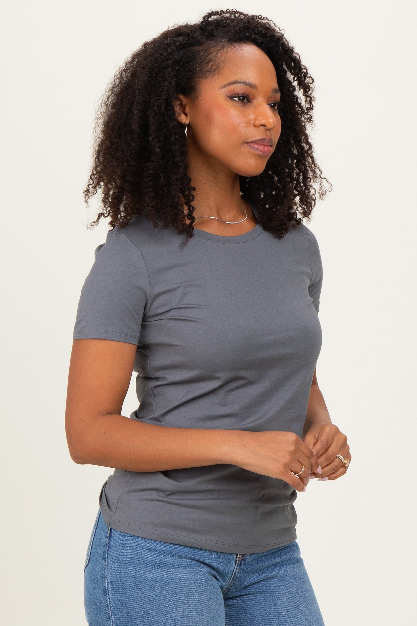 woman wearing a fitted gray short sleeve t-shirt and blue jeans, with curly hair and a side profile view