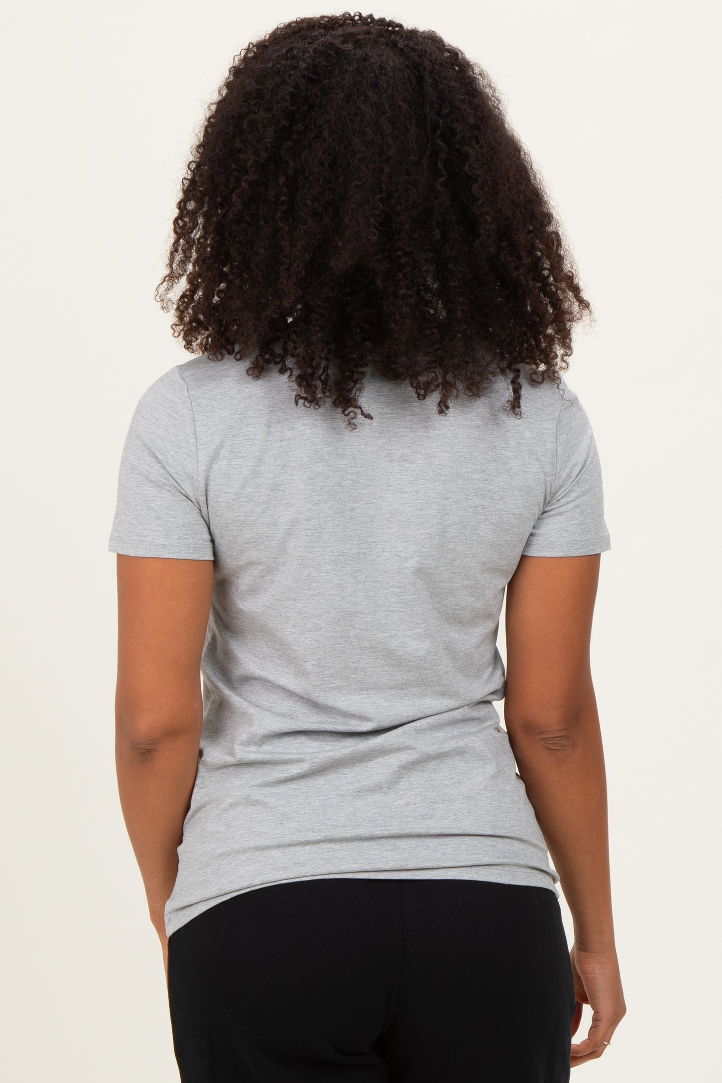 woman wearing a gray short sleeve t-shirt, seen from the back, with curly hair and black pants