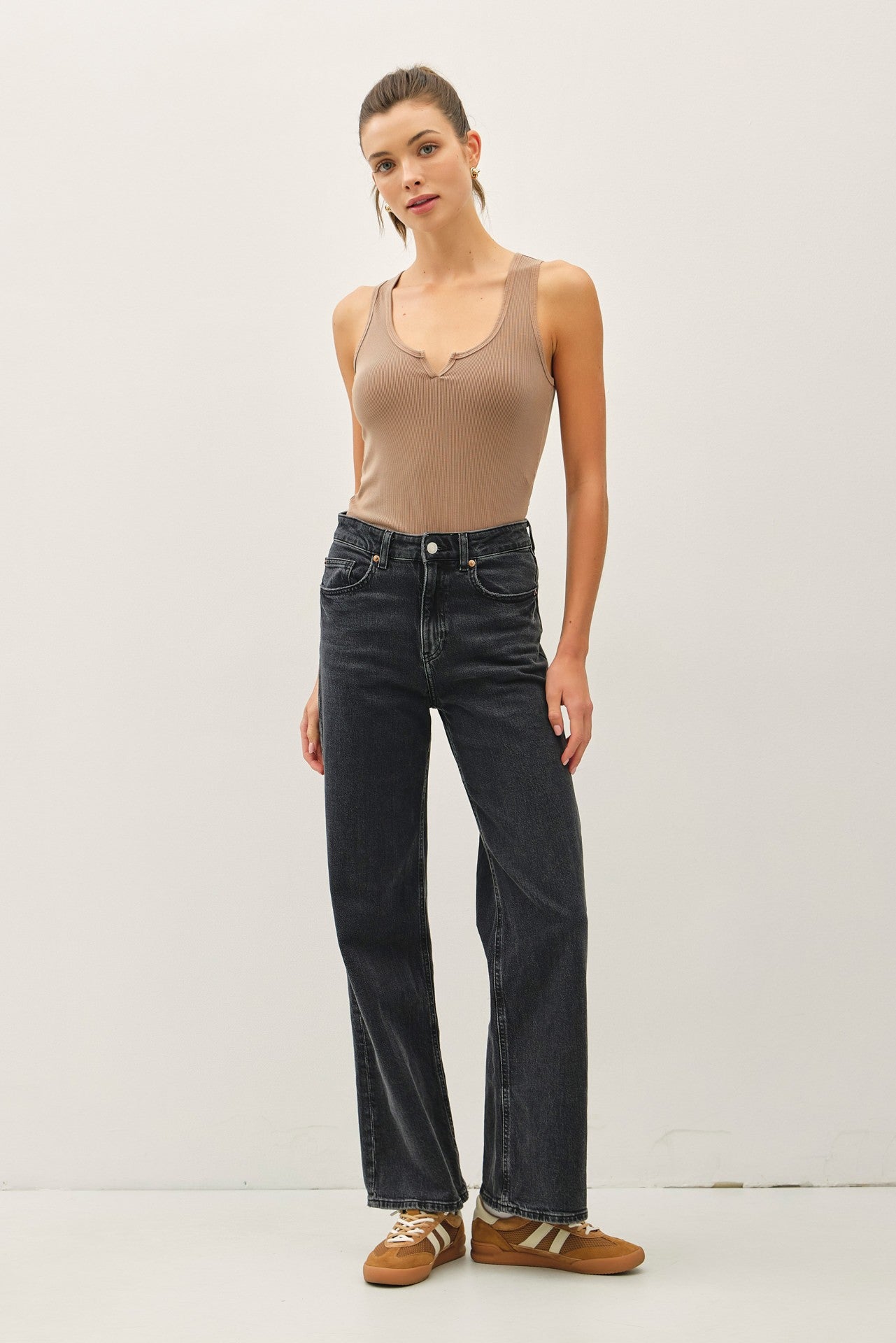 woman wearing a tan ribbed tank top and high-waisted black jeans with a relaxed fit, standing against a plain background