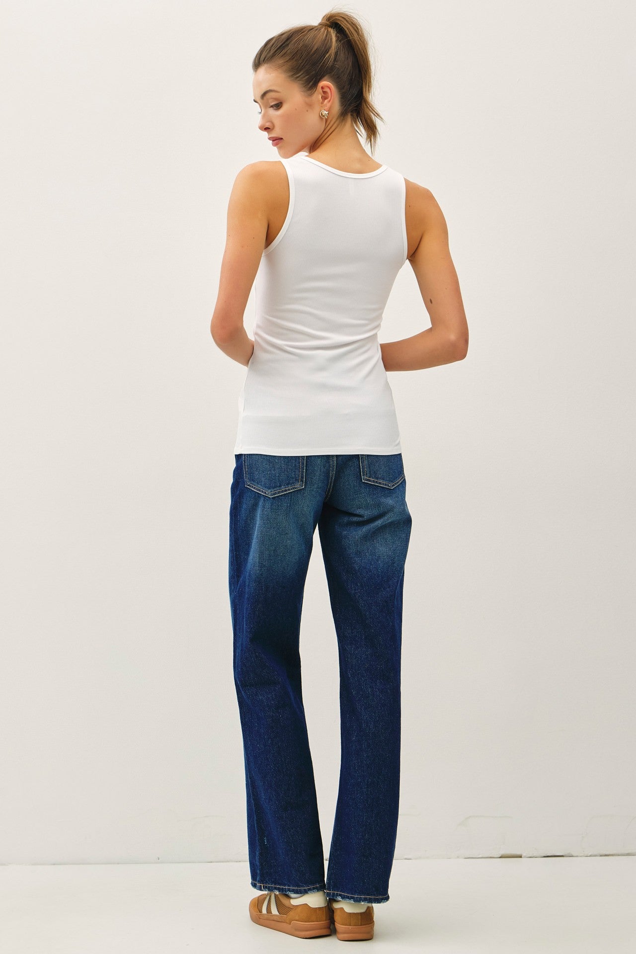 woman wearing a white sleeveless top and high-waisted blue denim jeans, viewed from the back