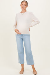 woman wearing a light beige long sleeve maternity sweater and blue cropped jeans, showing her baby bump