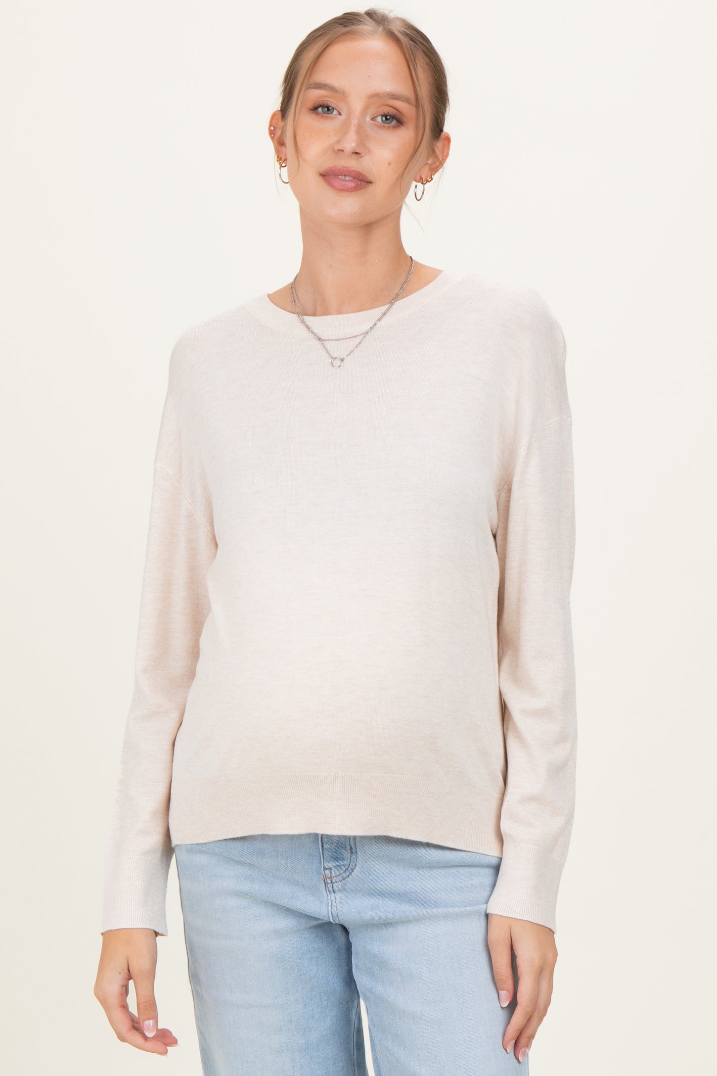 woman wearing a light beige maternity sweater with a relaxed fit and a visible baby bump, paired with light blue jeans