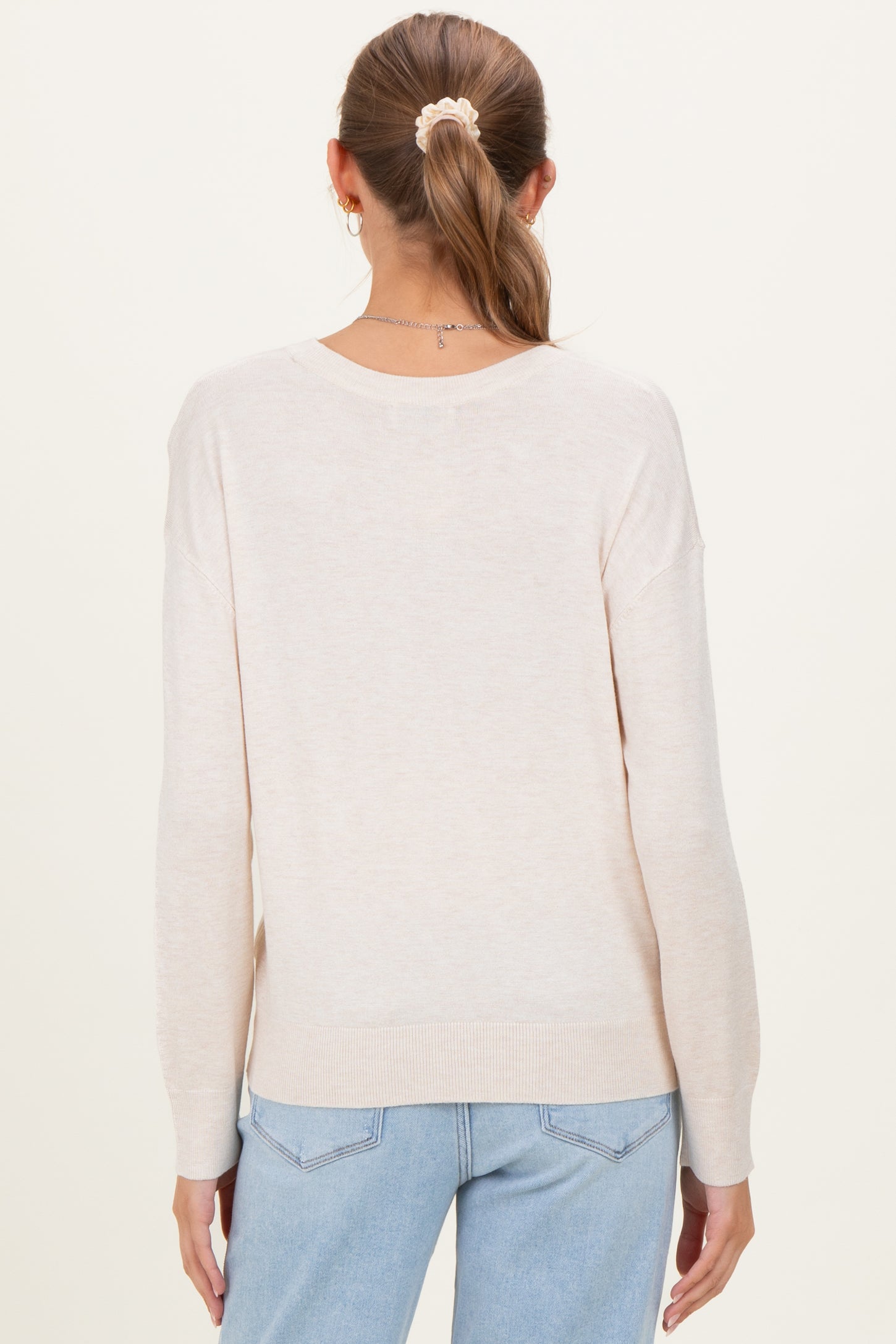 woman wearing a light beige maternity sweater with long sleeves and a relaxed fit, showing the back view.