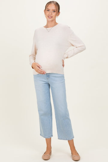 woman wearing a light beige long sleeve maternity sweater and blue cropped jeans, showing her baby bump