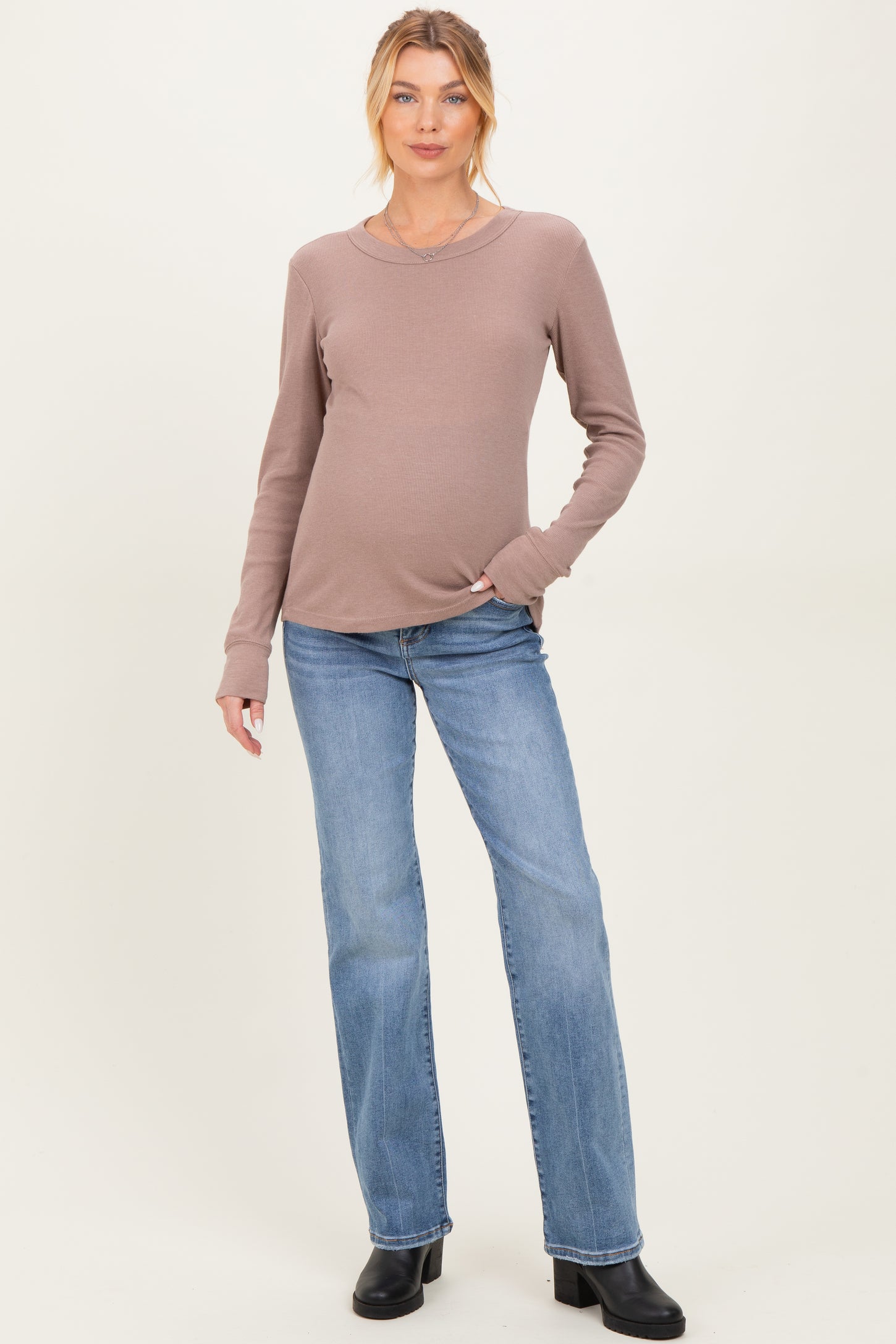 woman wearing a mauve long sleeve maternity top and blue flared jeans with a visible baby bump