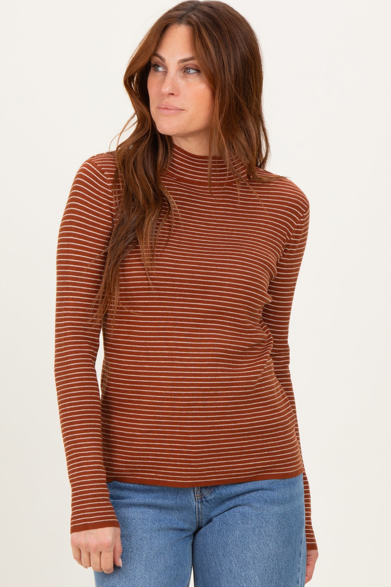 woman wearing a rust striped long sleeve top with a mock neck and paired with blue jeans
