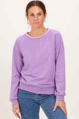 woman wearing a lavender crewneck sweatshirt with colorful stripe detailing and blue jeans