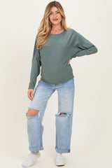 woman wearing a green long sleeve maternity top and distressed light blue jeans, showing her baby bump