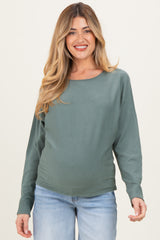 woman wearing a green long sleeve maternity sweater and showing her baby bump