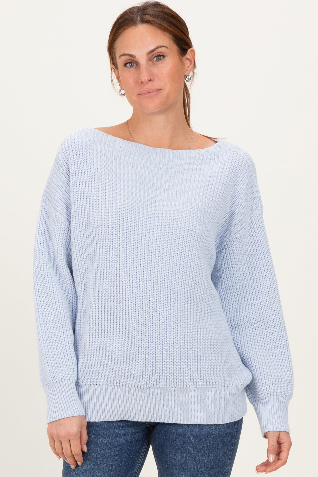 woman wearing a light blue oversized knit sweater with a wide neckline and long sleeves, paired with jeans