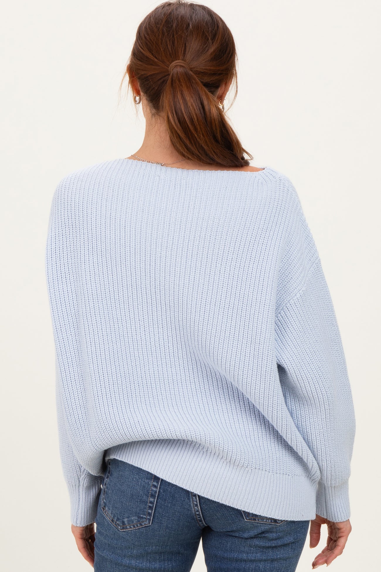 woman wearing a light blue oversized knit sweater from the back with a relaxed fit and wide neckline