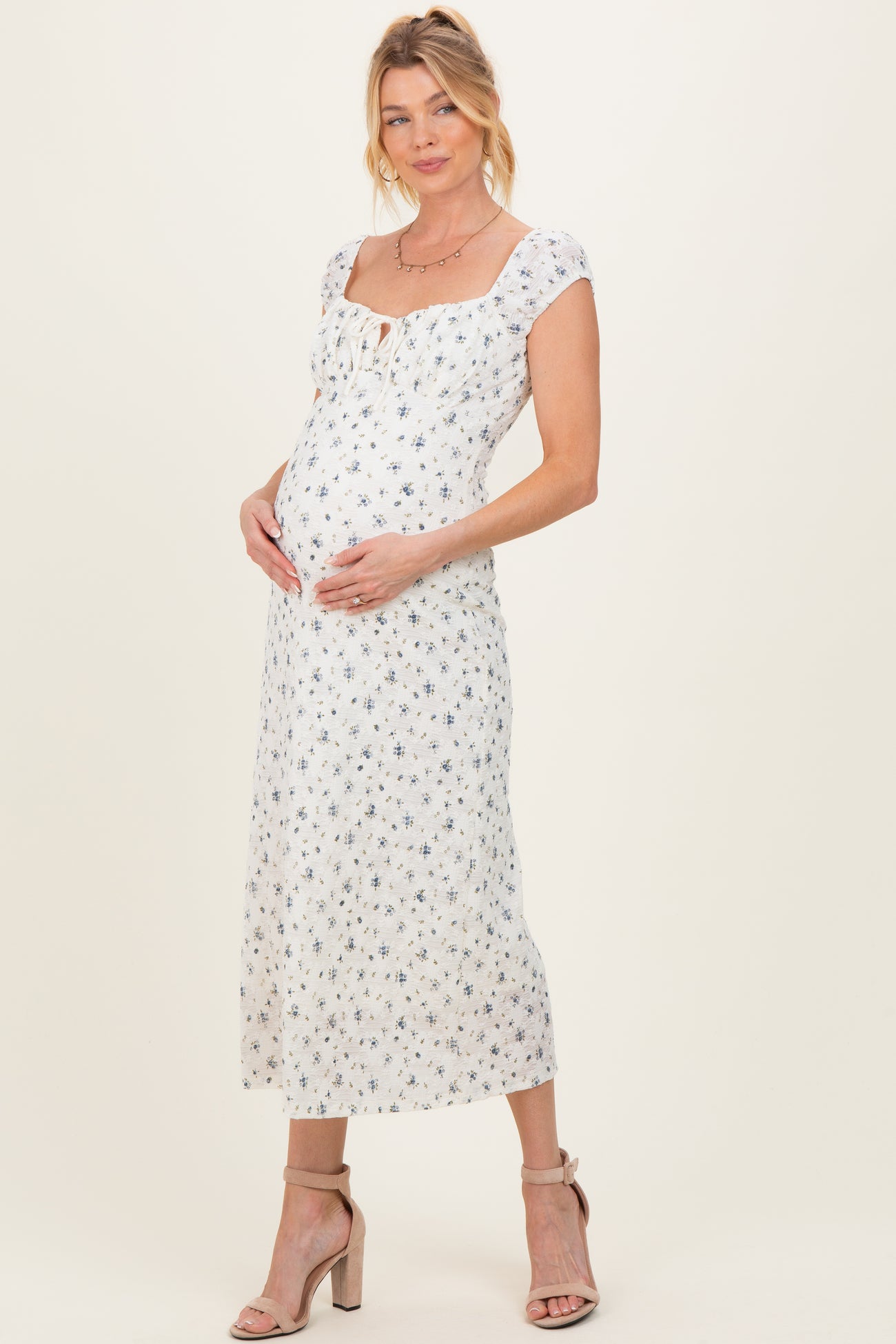 woman wearing a white floral maternity dress with a square neckline and short sleeves, cradling her baby bump