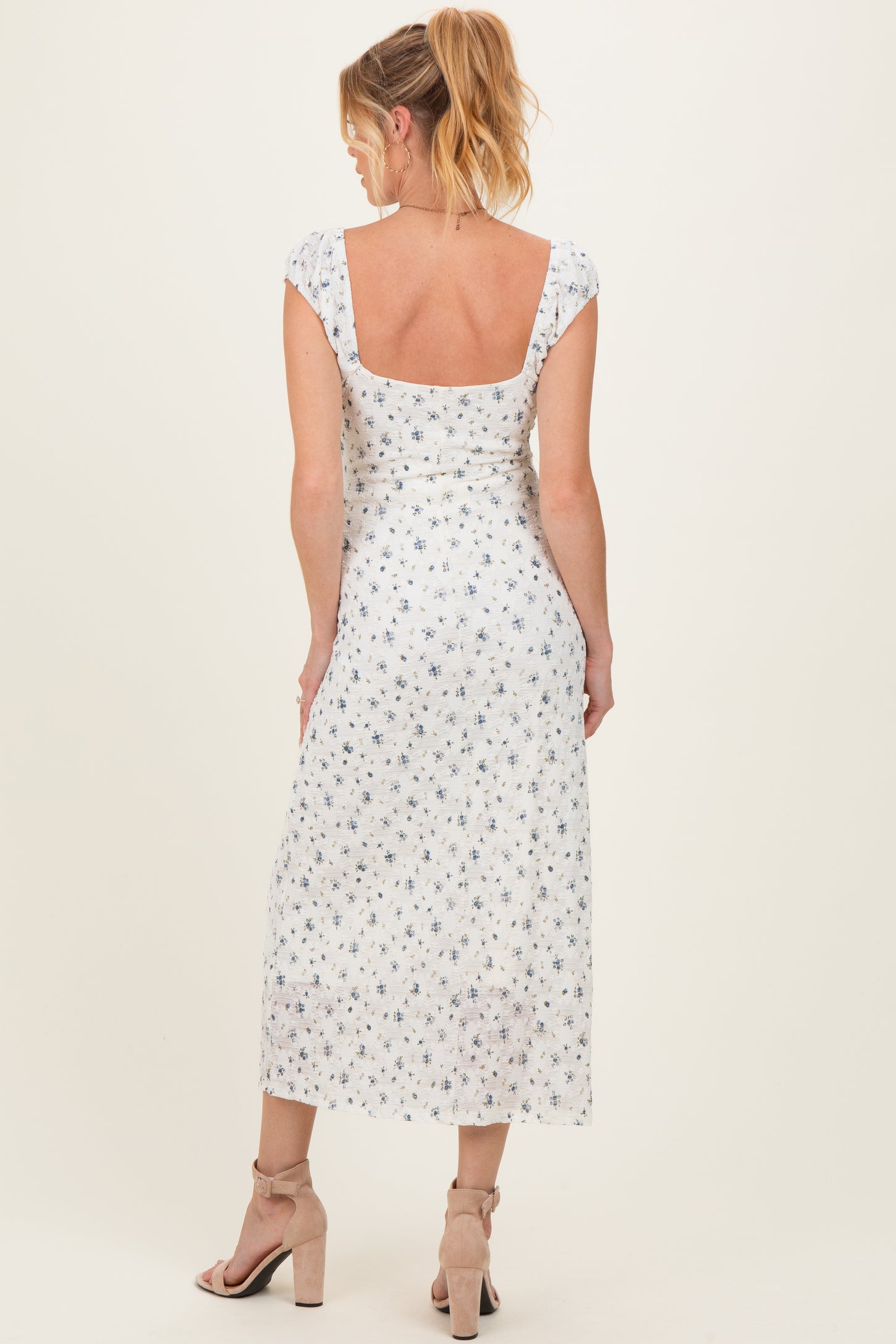 woman wearing a white maternity dress with blue floral print and short sleeves, shown from the back