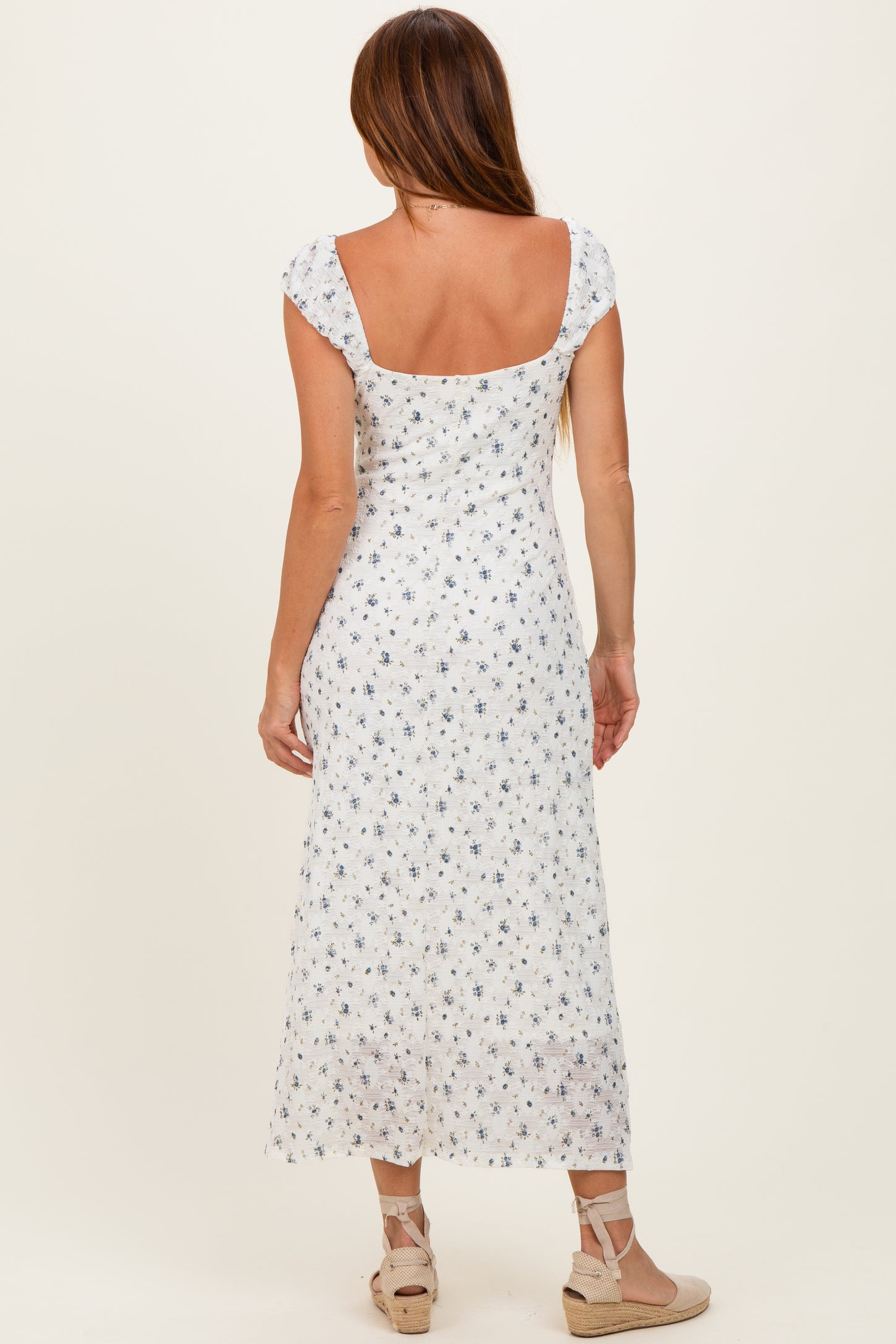 woman wearing a white floral maxi dress, view is from the back, showing cap sleeves and a low scoop neckline