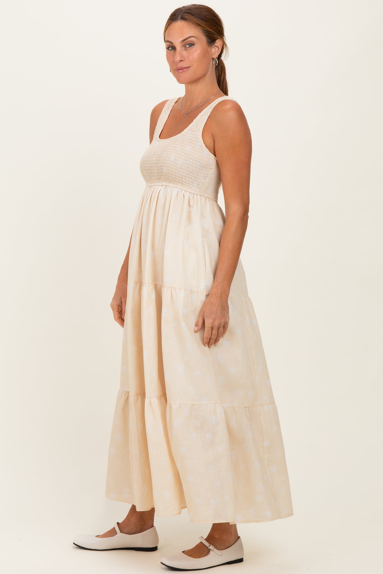 woman wearing a cream maxi dress with a tiered skirt and a fitted bodice, styled with white slip-on shoes