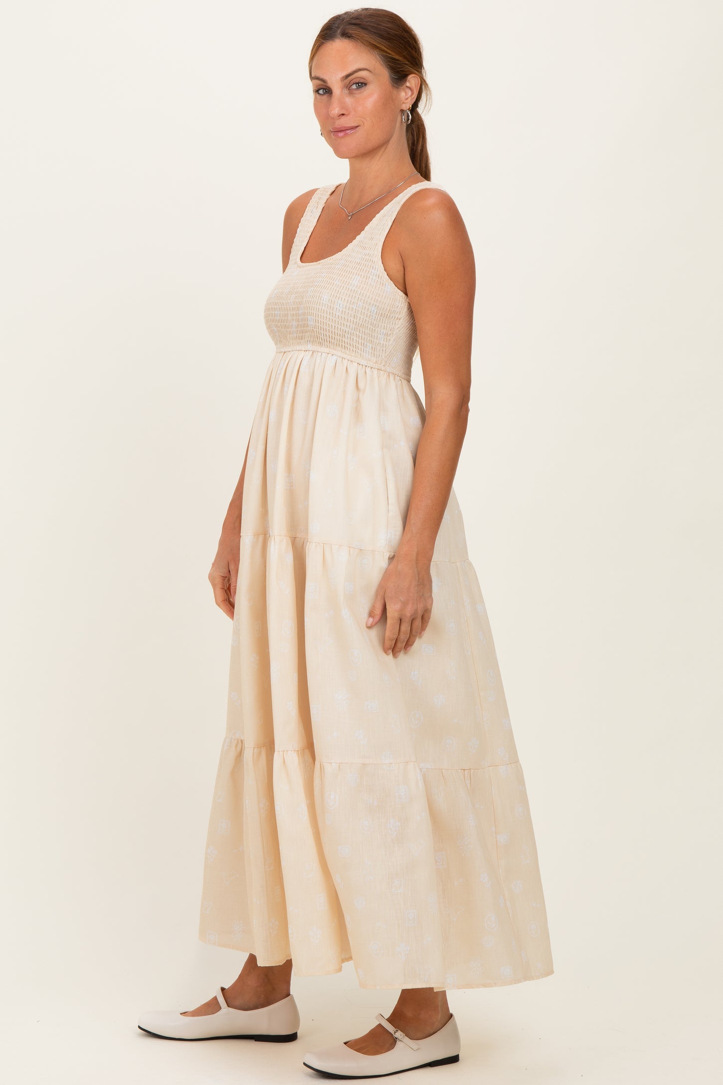 woman wearing a cream maxi dress with a tiered skirt and a fitted bodice, styled with white slip-on shoes