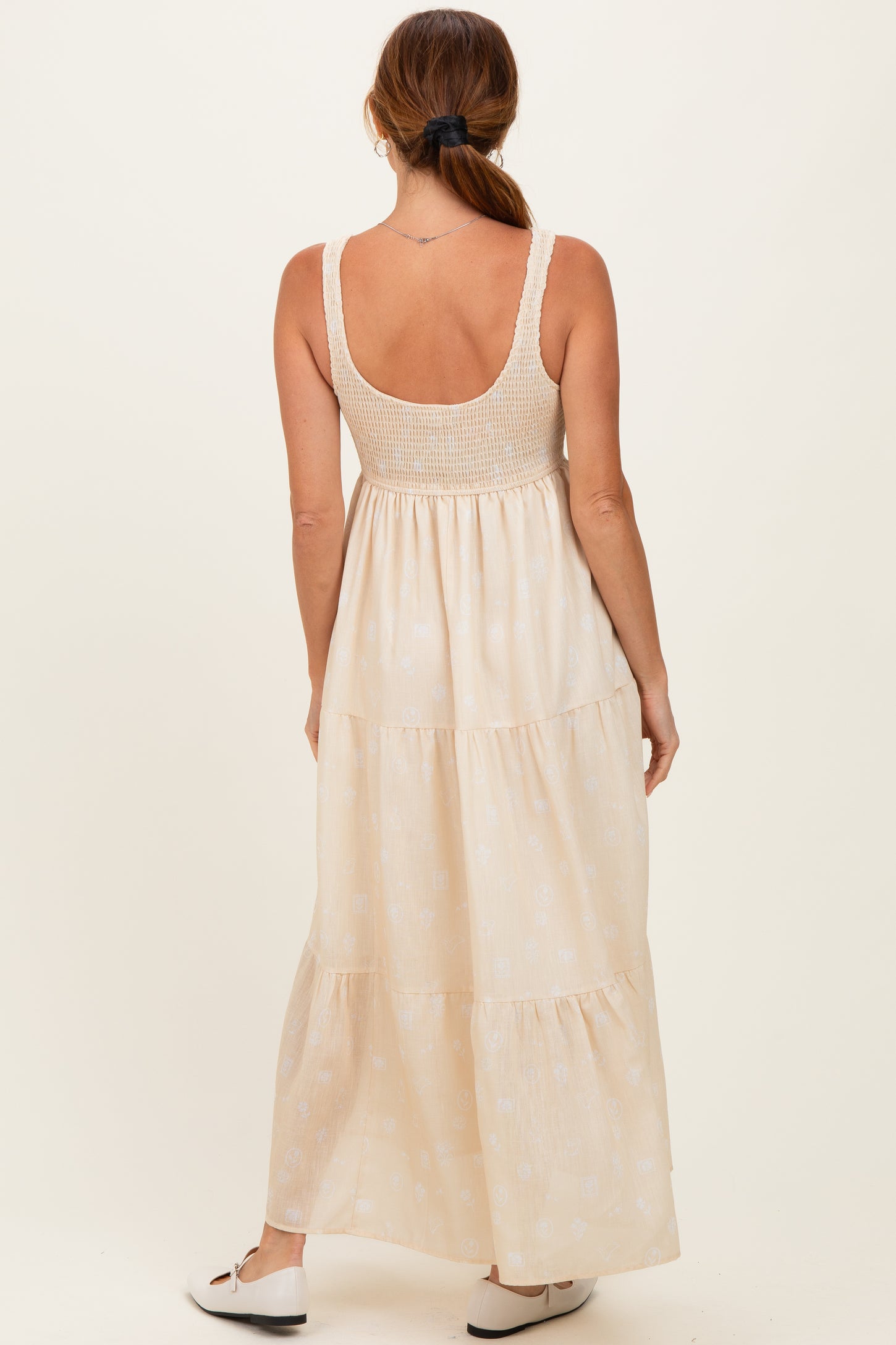 woman wearing a backless cream maxi dress with a smocked bodice and tiered skirt, standing against a neutral background