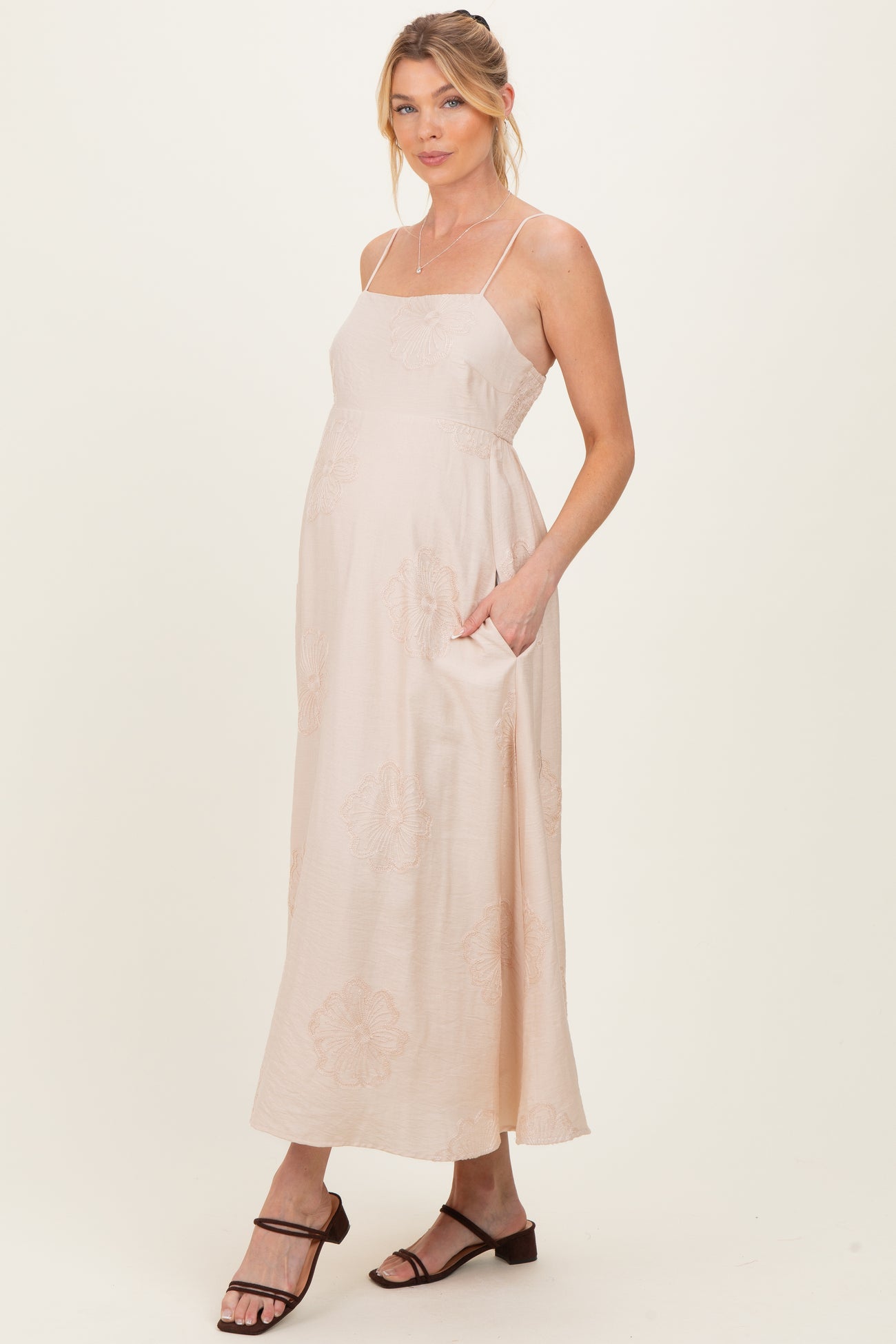 woman wearing a light pink maternity maxi dress with spaghetti straps and side pockets, showcasing her baby bump