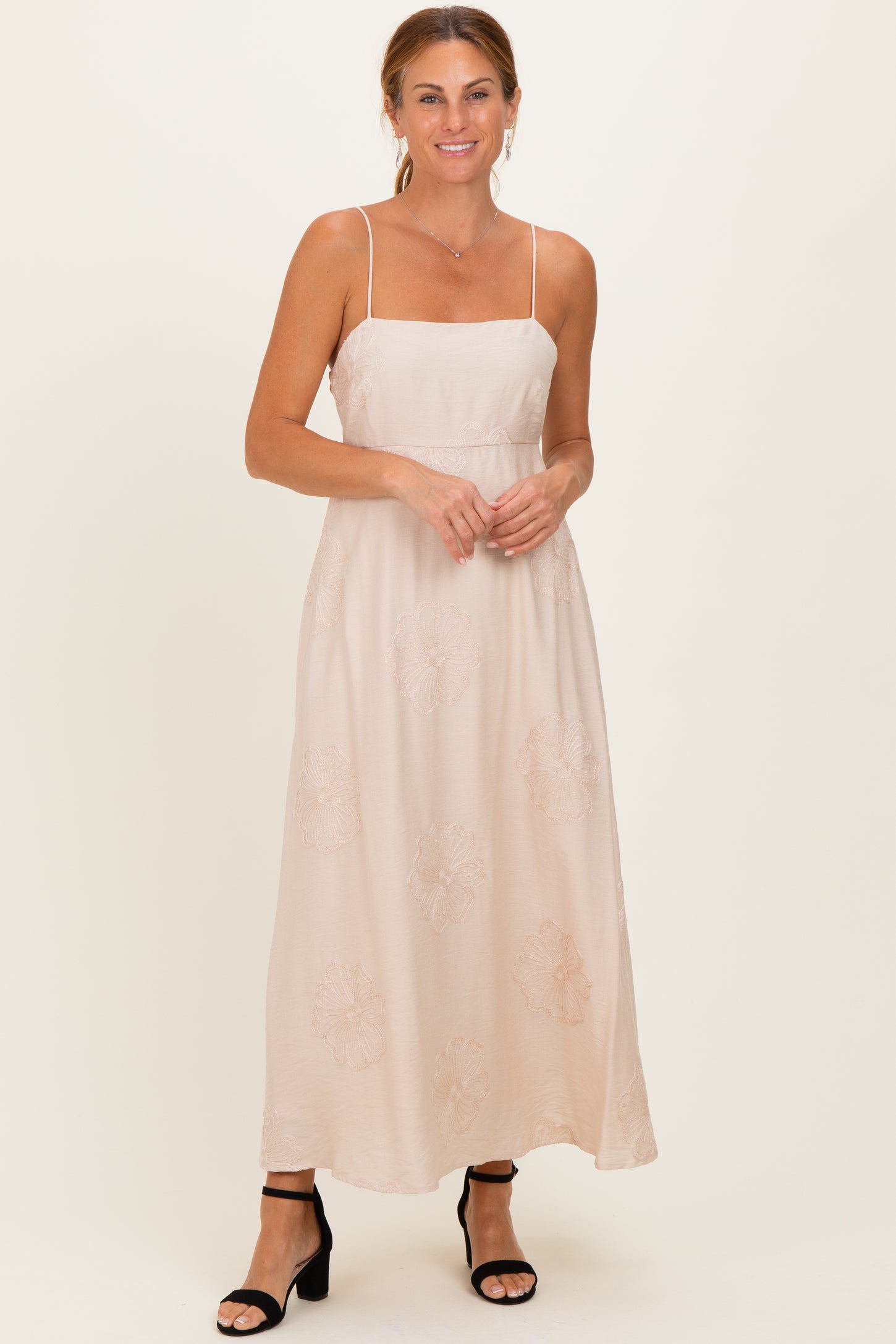 woman wearing a blush pink maxi dress with spaghetti straps and floral embroidery details