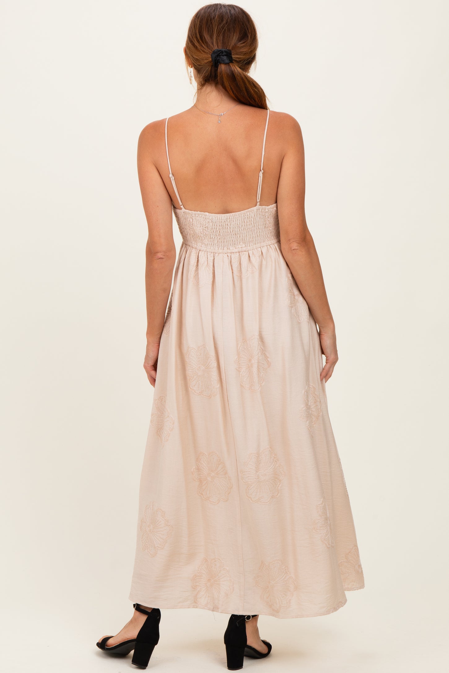 woman wearing a light pink maxi dress with spaghetti straps and a smocked bodice, showing floral details
