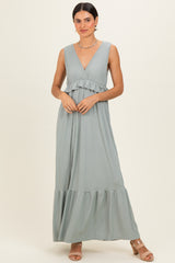 woman wearing a light green maxi dress with a ruffled bodice and v-neckline, standing against a neutral background