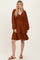 woman wearing a rust colored long sleeve mini dress with a smocked bodice and ruffled hem, styled with brown sandals