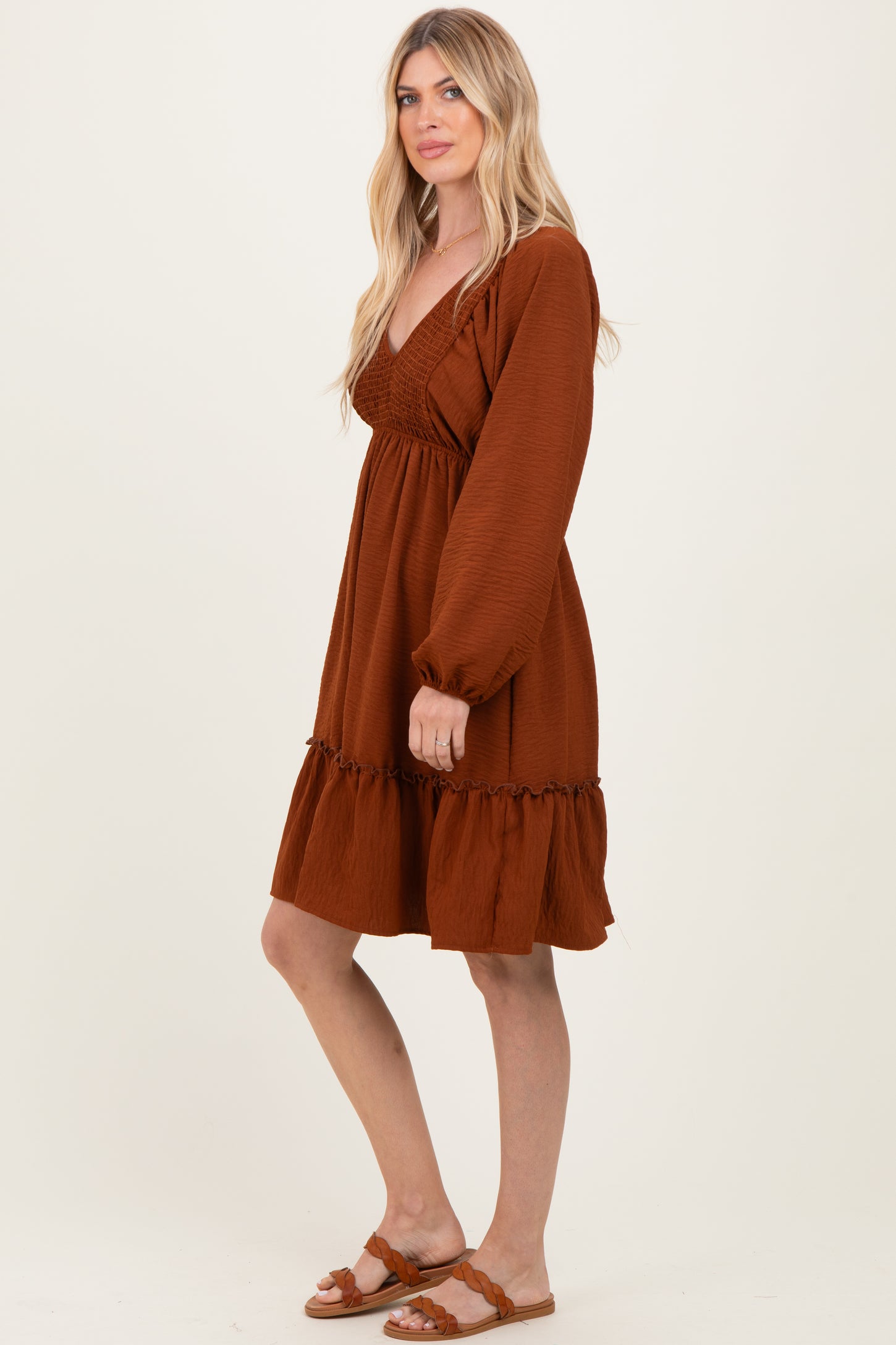 woman wearing a rust-colored long sleeve dress with a smocked bodice and ruffled hem, standing sideways
