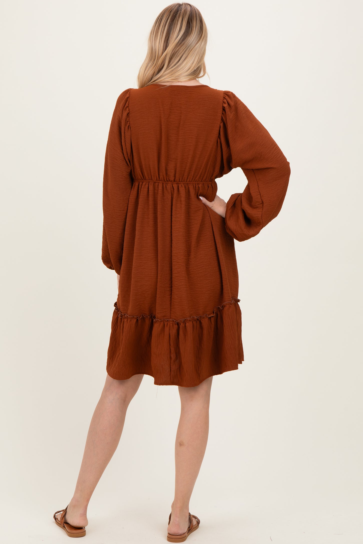 woman wearing a rust-colored long sleeve dress with a tiered ruffle hem and elastic waistband, seen from the back
