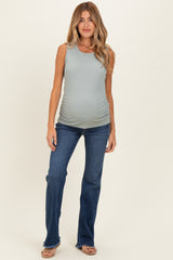 woman wearing a light green ribbed maternity tank top and blue flared jeans, showing her baby bump