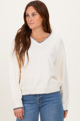 woman wearing a cream v-neck sweater with navy trim and relaxed fit, styled with light blue jeans