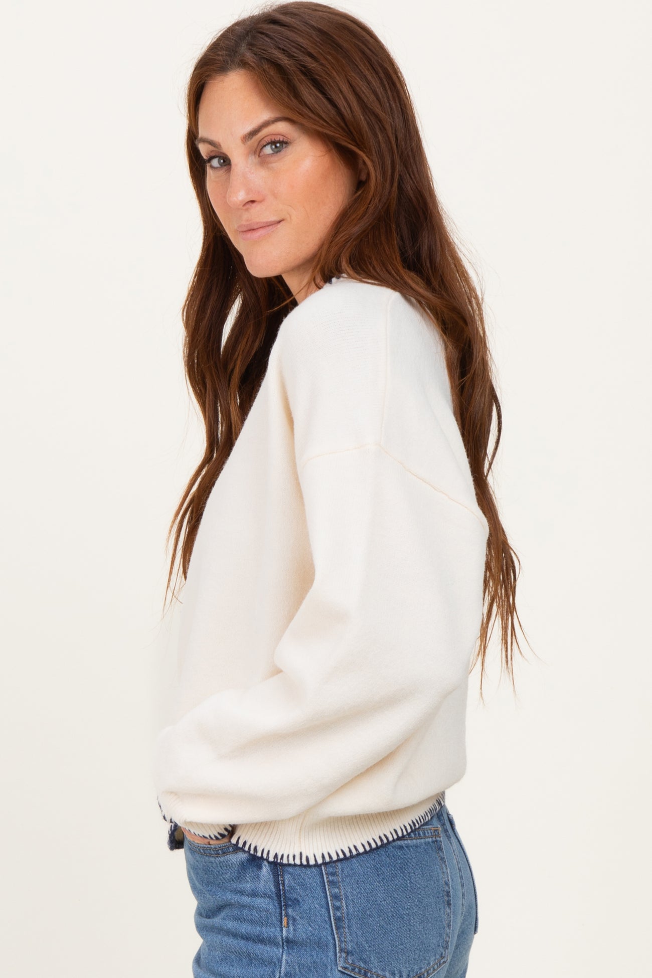 woman wearing a cream-colored oversized sweatshirt with ribbed detailing and blue denim jeans