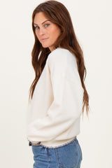 woman wearing a cream-colored oversized sweatshirt with ribbed detailing and blue denim jeans