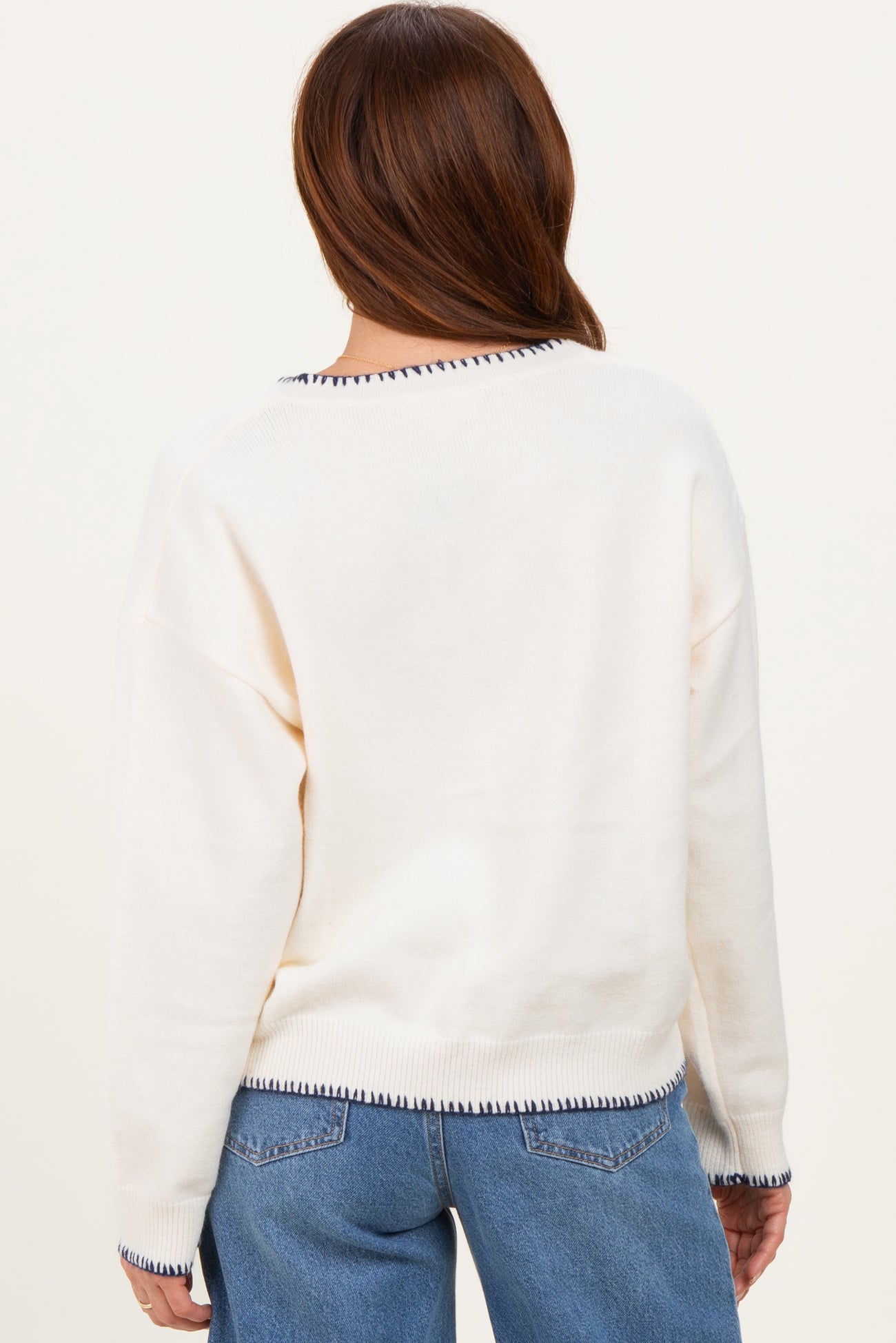 woman wearing a cream oversized sweater with navy trim, styled with light blue jeans, back view