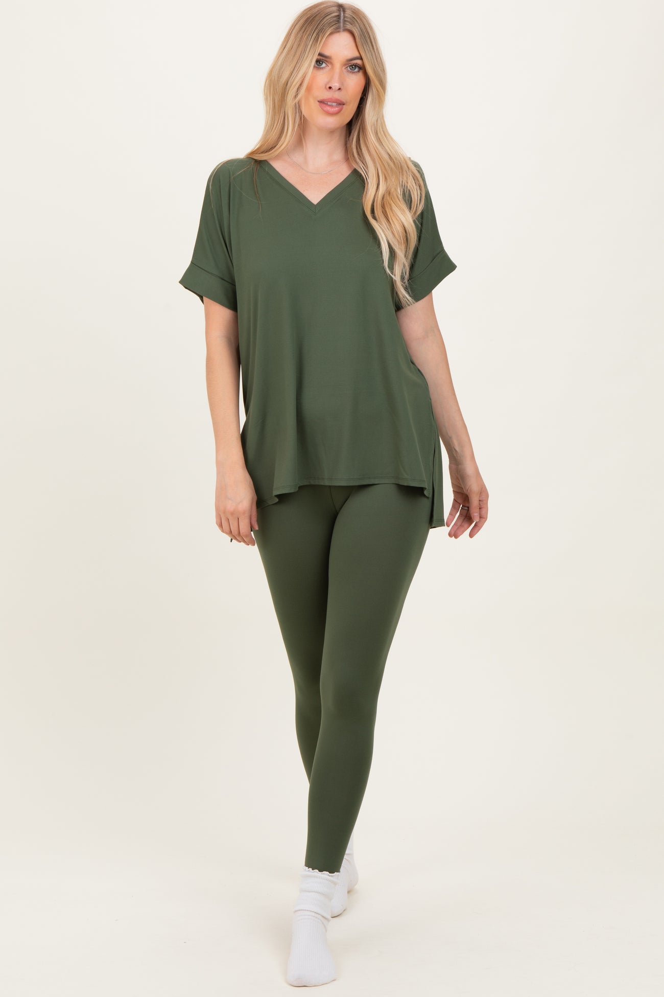 woman wearing an olive green oversized v-neck top and matching leggings, standing on white background