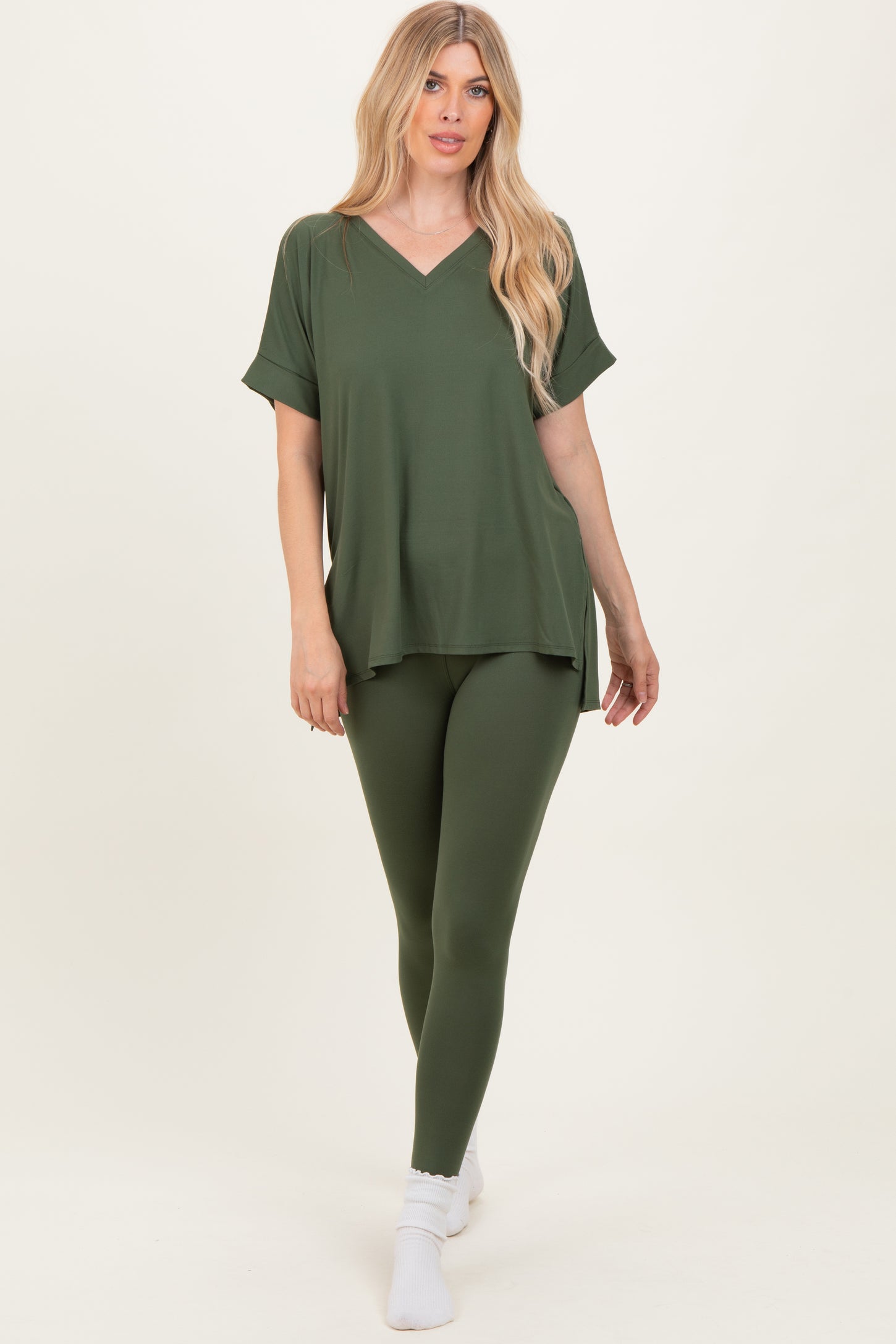 woman wearing an olive green oversized v-neck top and matching leggings, standing on white background