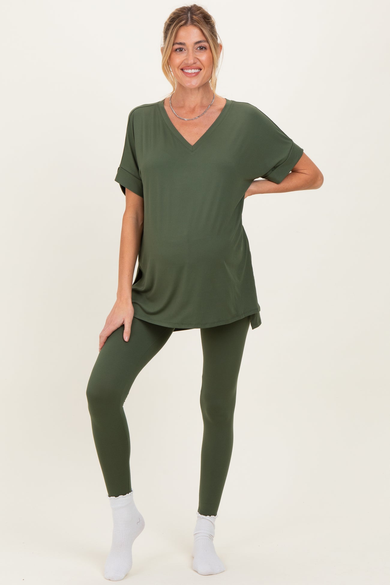 woman wearing a dark green maternity top and matching leggings, showing her baby bump with a relaxed fit
