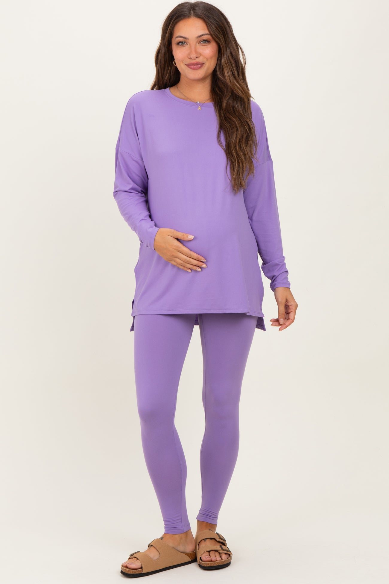 woman wearing a purple long sleeve maternity top and matching leggings, holding her baby bump