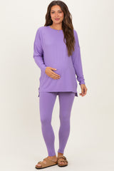 woman wearing a purple long sleeve maternity top and matching leggings, holding her baby bump