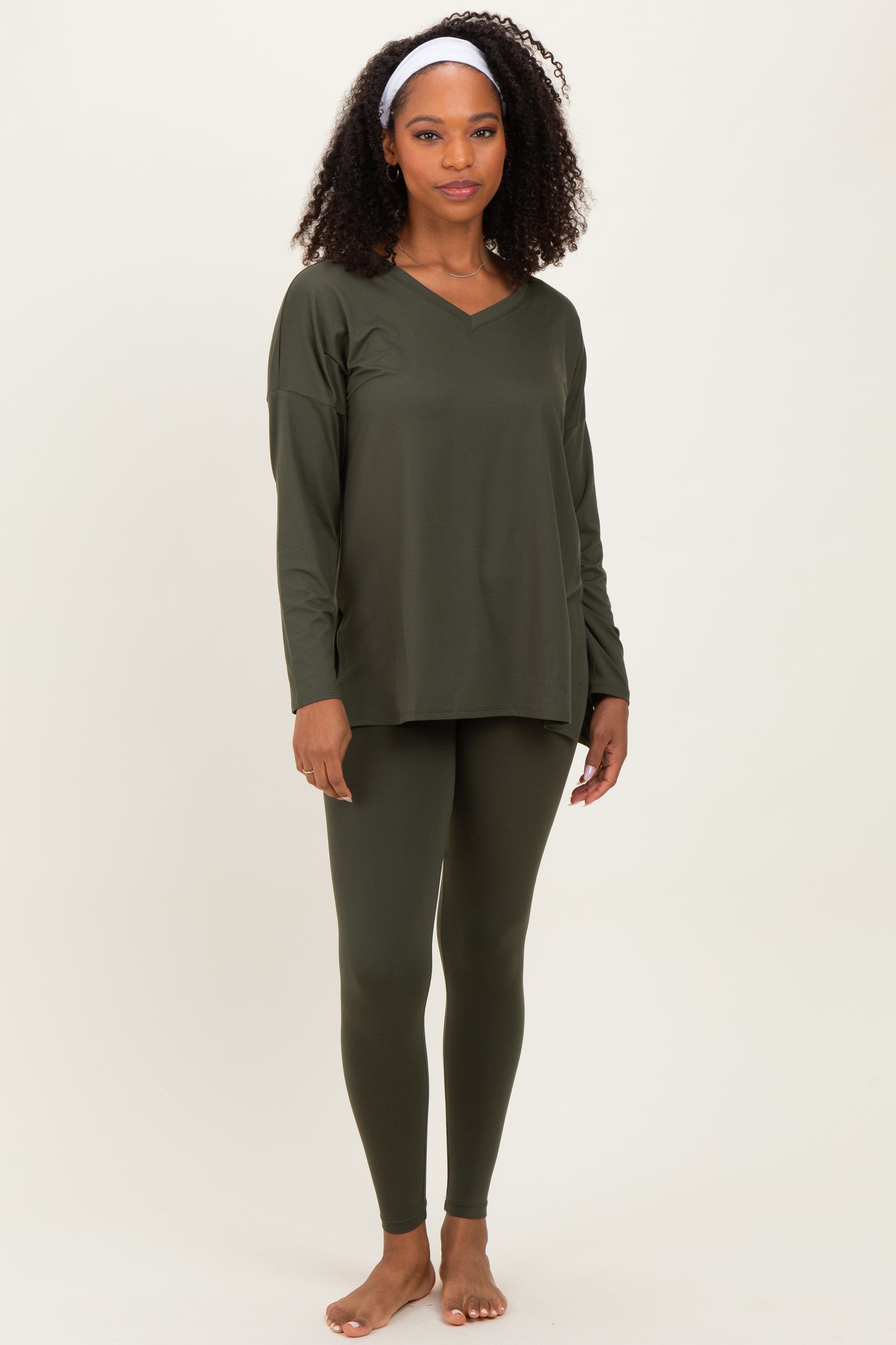 woman wearing an olive green long sleeve top and matching leggings, standing barefoot with a headband