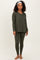 woman wearing an olive green long sleeve top and matching leggings, standing barefoot with a headband