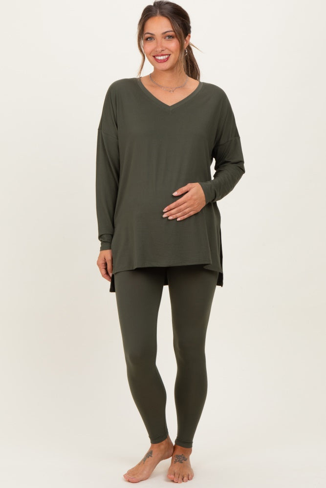woman wearing a dark green maternity top and matching leggings, gently cradling her baby bump