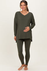 woman wearing a dark green maternity top and matching leggings, gently cradling her baby bump